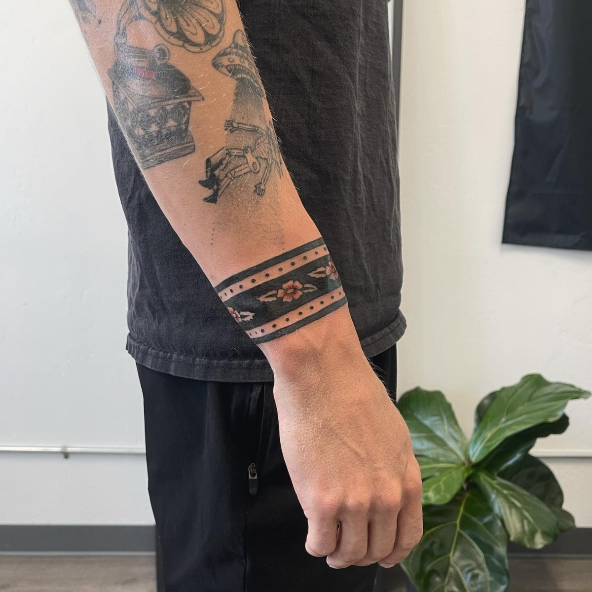 A person's forearm displaying a black and tan American traditional floral band tattoo.