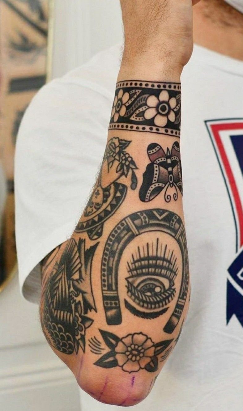 A person's arm displaying various black ink tattoos including floral bands, a butterfly, and a horseshoe.