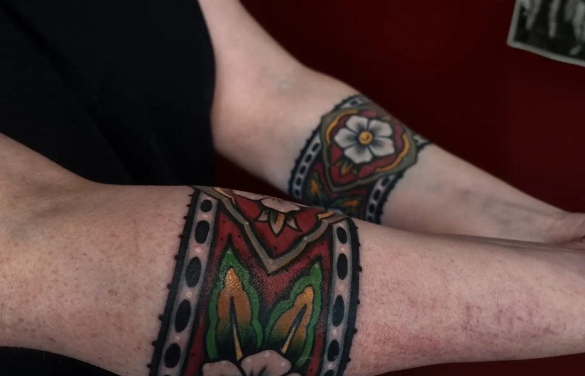 Two arms displaying matching American traditional floral band tattoos with red and green accents.