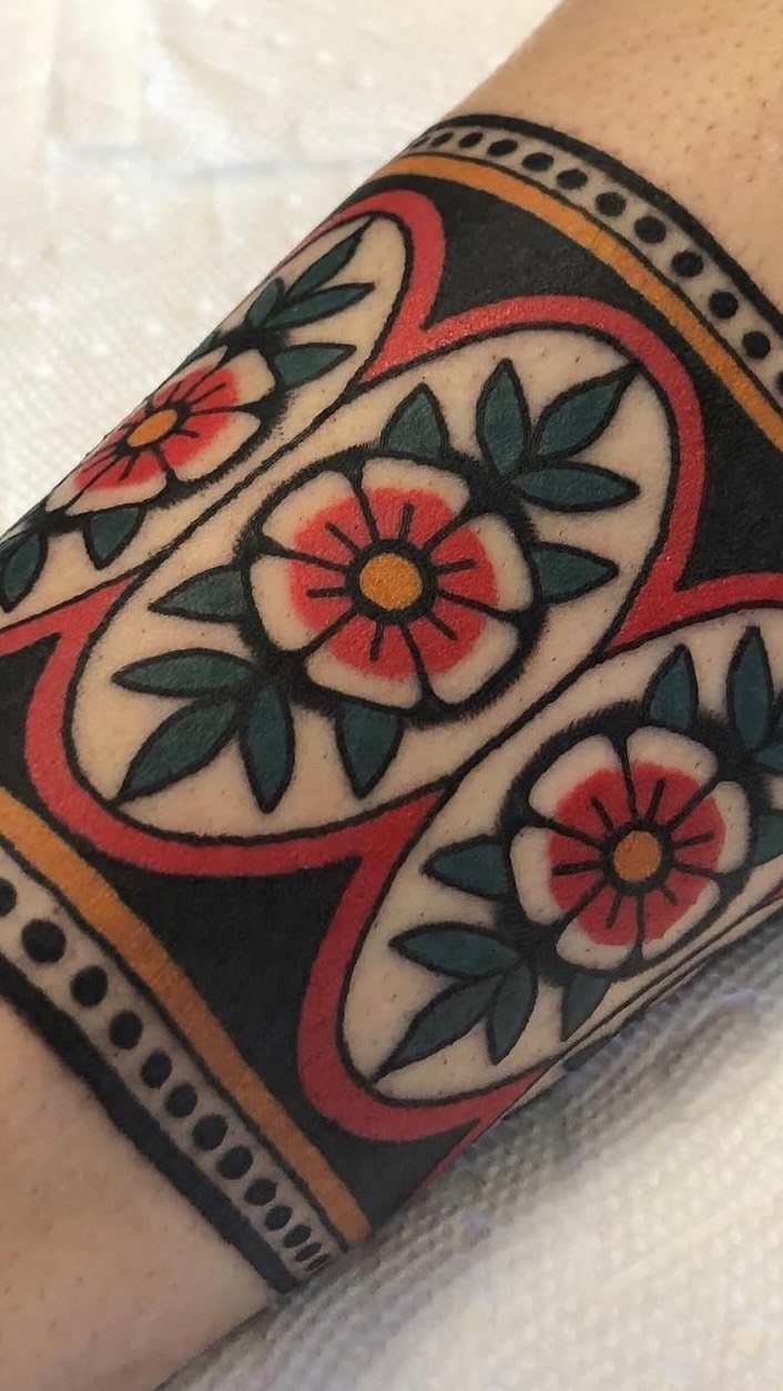 An American traditional arm band tattoo featuring red flowers and green leaves on a person's arm.