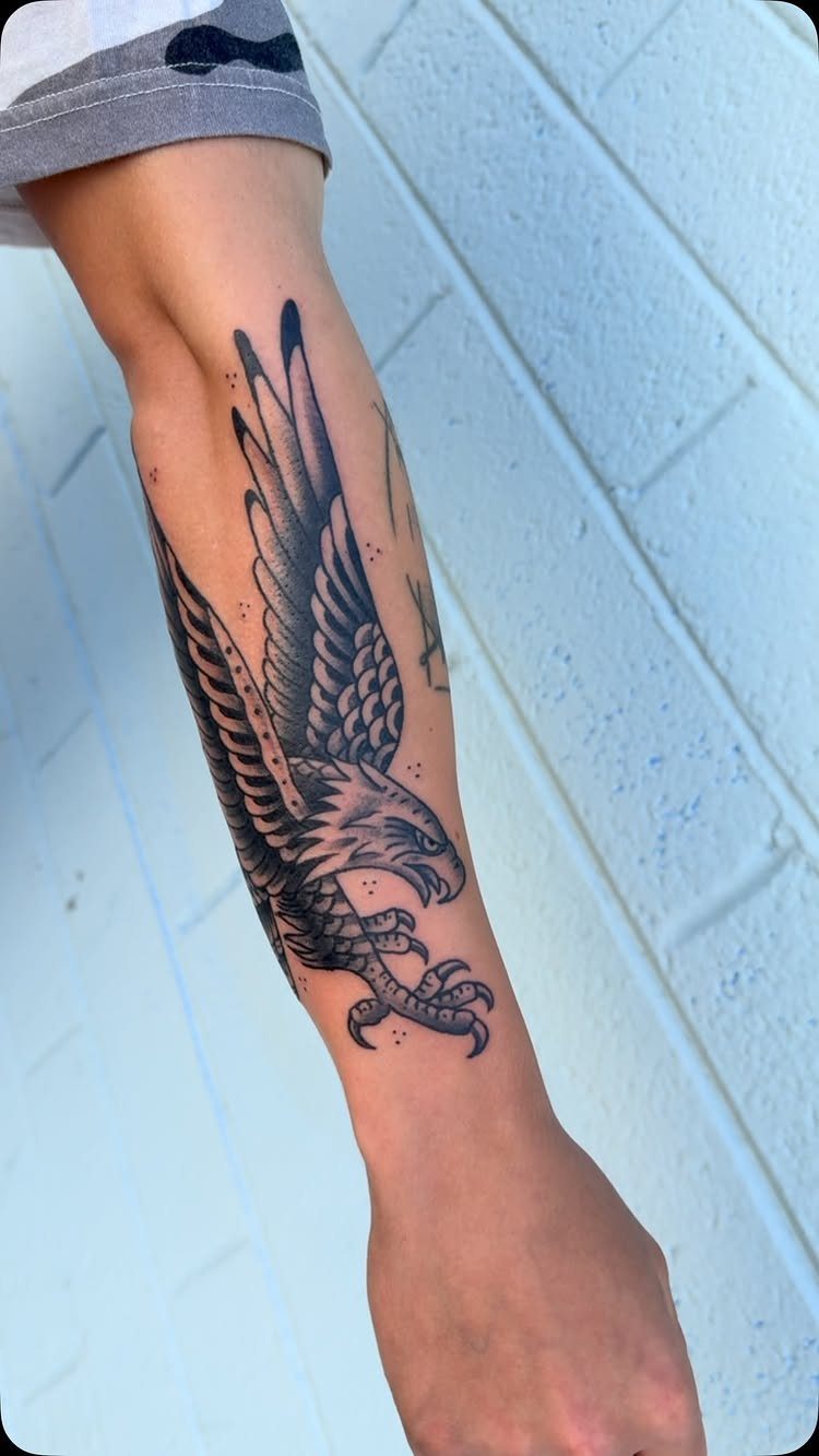 A black and grey eagle tattoo with spread wings on a person's forearm.
