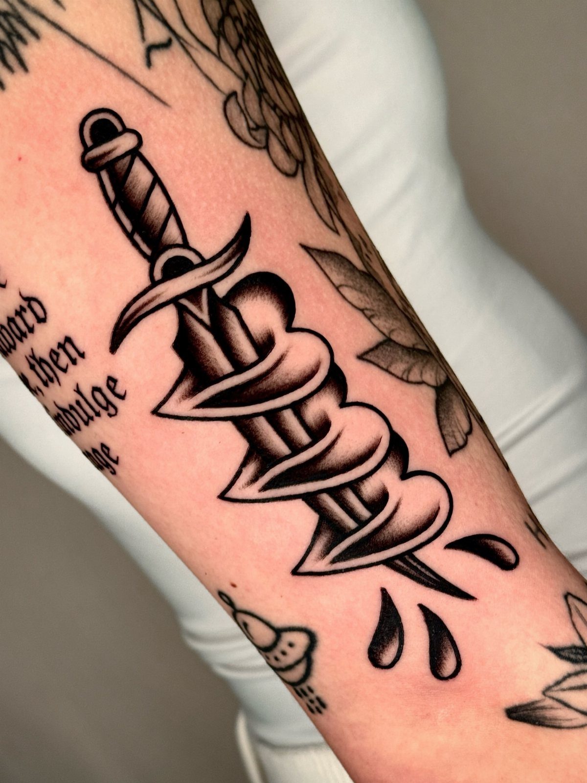 A black and grey tattoo of a dagger piercing through a heart on a person's arm.