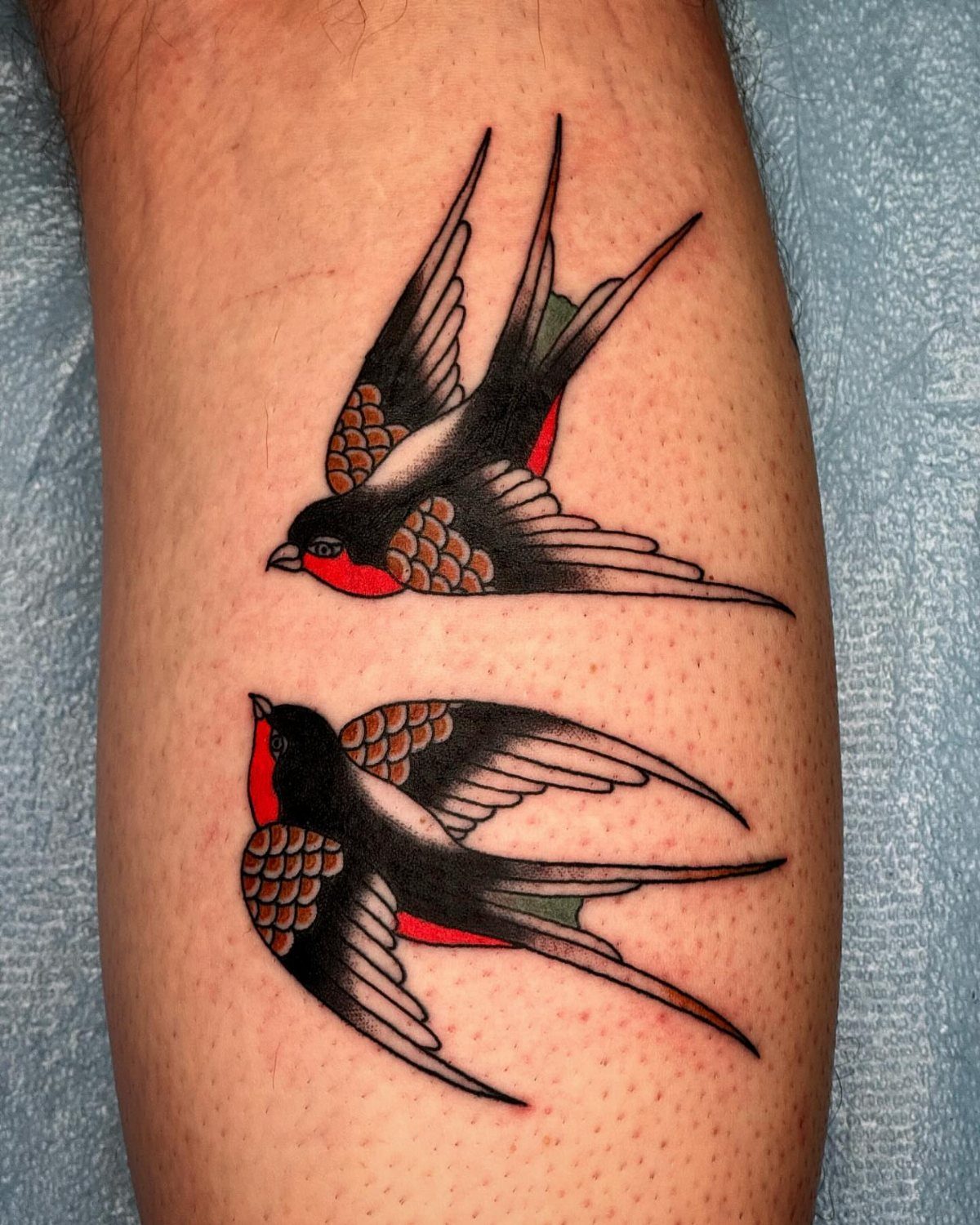 Two traditional swallow tattoos with black and red ink on a person's skin.