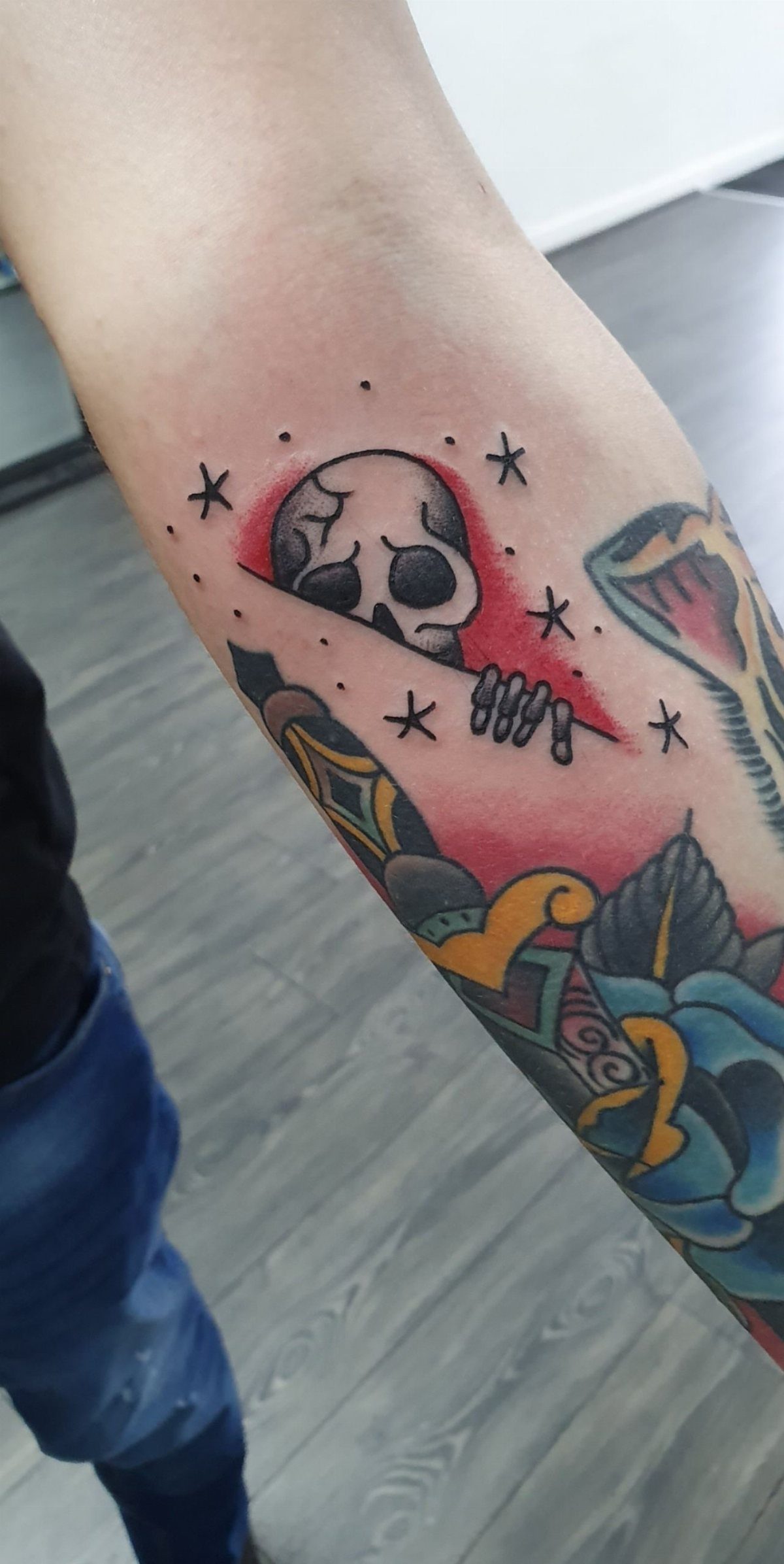 8 Arm Tattoo Filler Ideas for Sleeves That Actually Work 5 A person's arm displaying a skull tattoo surrounded by small black stars and dots.
