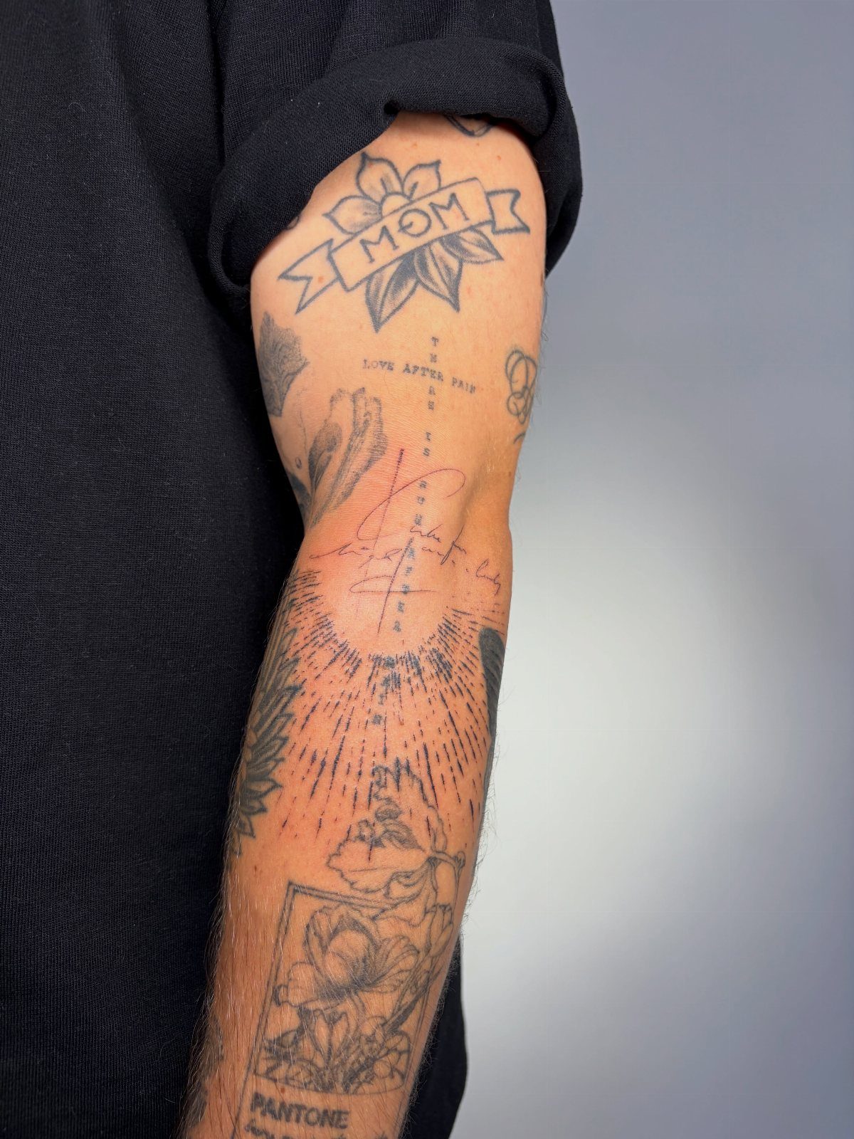 8 Arm Tattoo Filler Ideas for Sleeves That Actually Work 7 A person's arm covered in various black ink tattoos including flowers, a sunburst, and text.