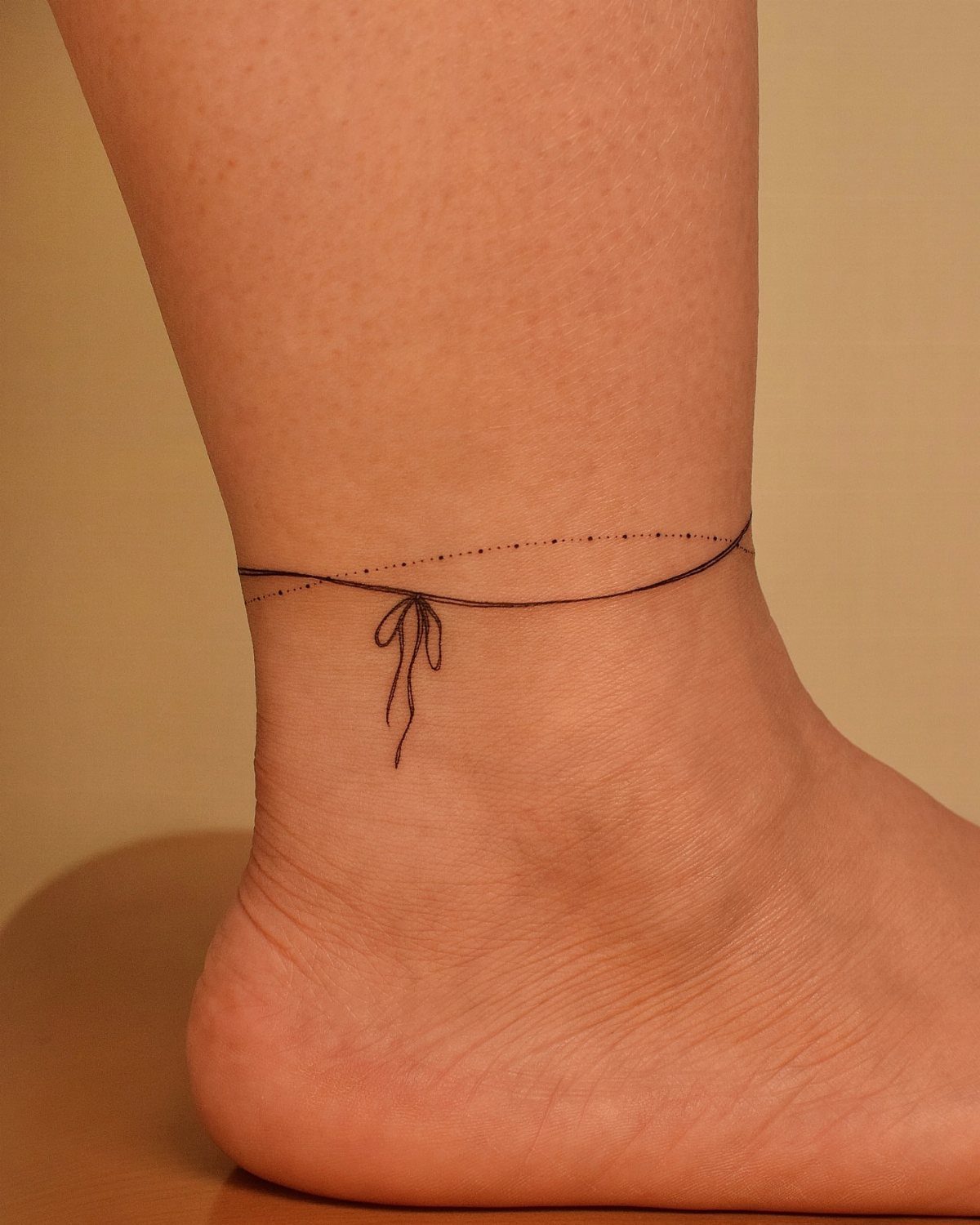 10 Around Ankle Tattoo Ideas That Follow the Body's Line 10 A fine-line black ink tattoo of a delicate string and bow wrapped around a person's ankle.