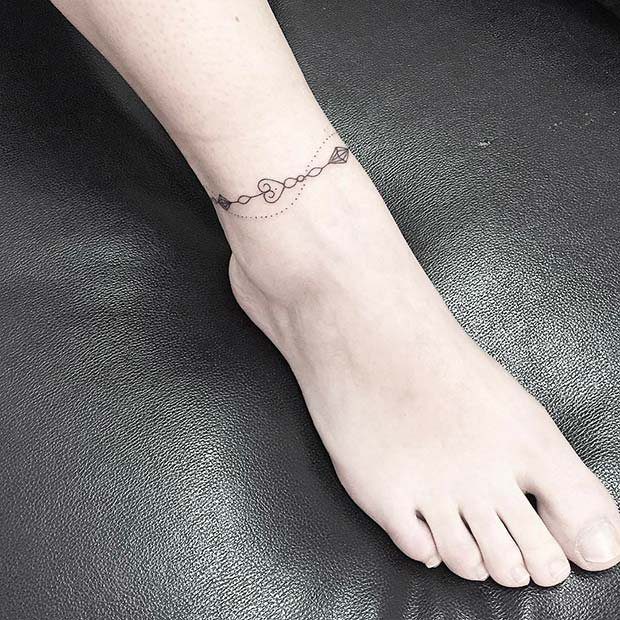10 Around Ankle Tattoo Ideas That Follow the Body's Line 8 A person's ankle featuring a delicate fine-line geometric and heart tattoo encircling the skin.