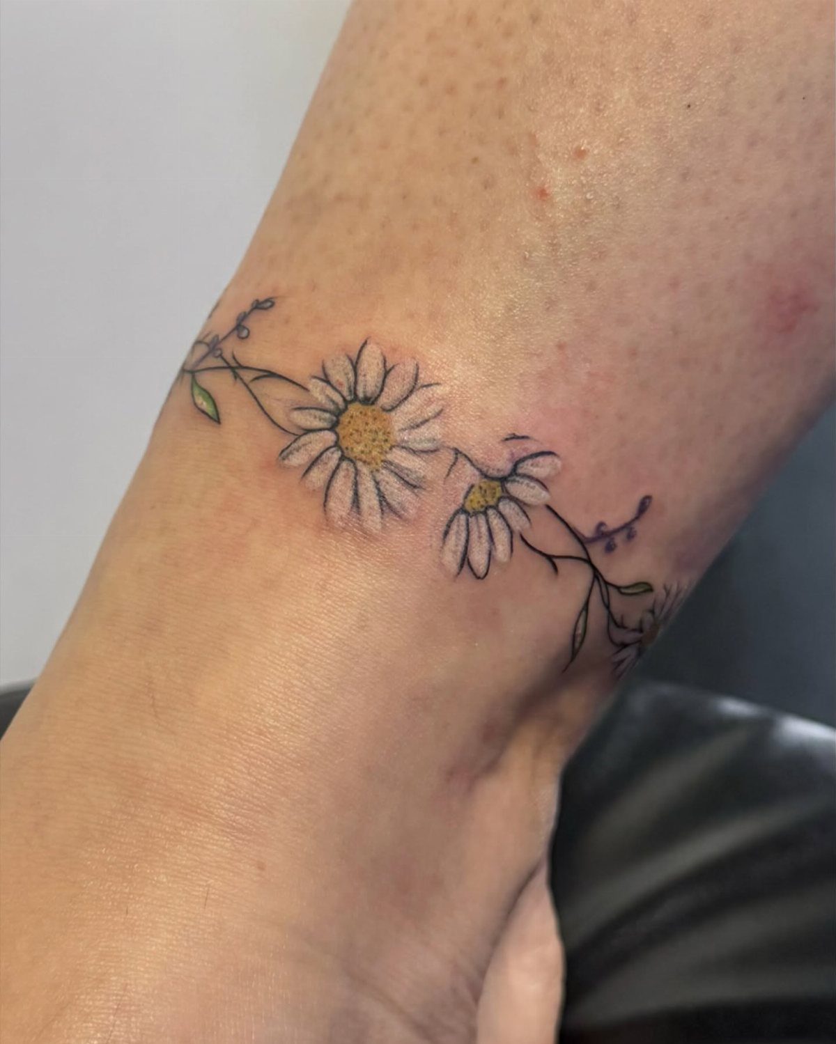 10 Around Ankle Tattoo Ideas That Follow the Body's Line 6 A daisy and vine tattoo wrapping around a person's ankle skin.