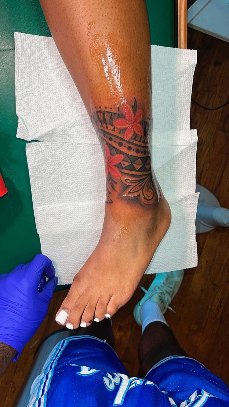 10 Around Ankle Tattoo Ideas That Follow the Body's Line 2 A tribal style tattoo with red flowers wrapped around a person's ankle and lower leg.