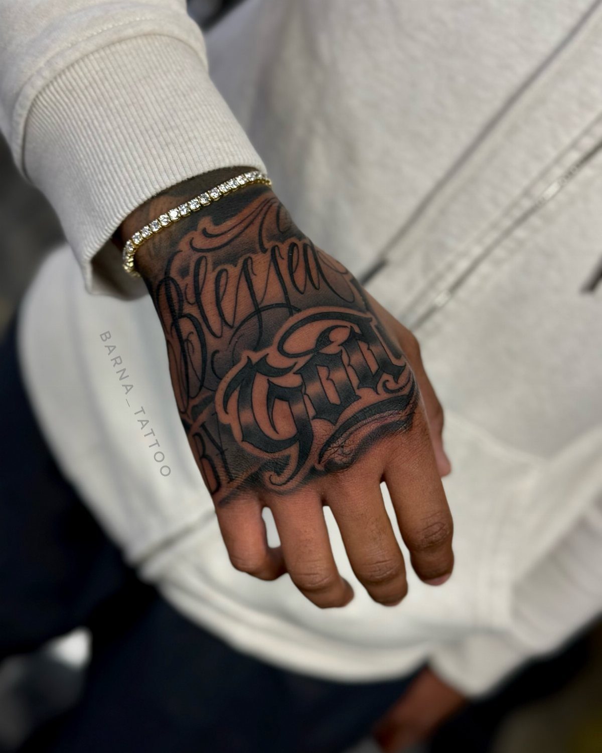 A hand with a large black script tattoo reading Blessed God on the back.