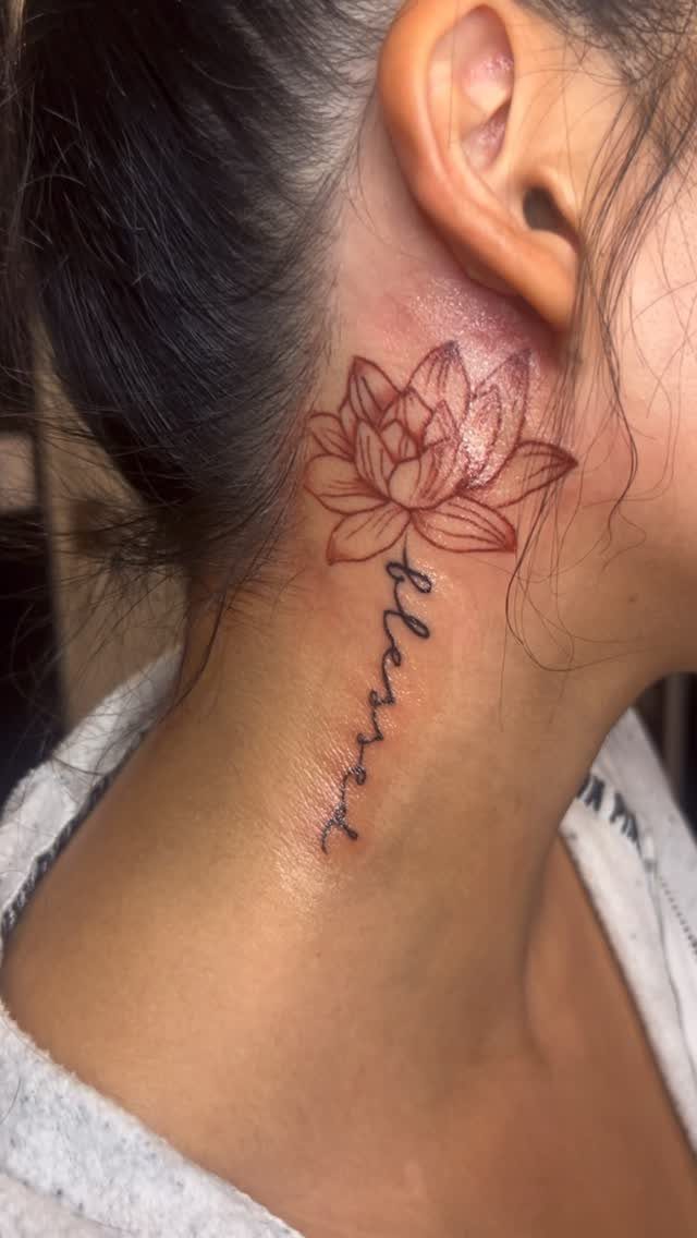 A red ink lotus flower tattoo with the word blessed written underneath on a neck.