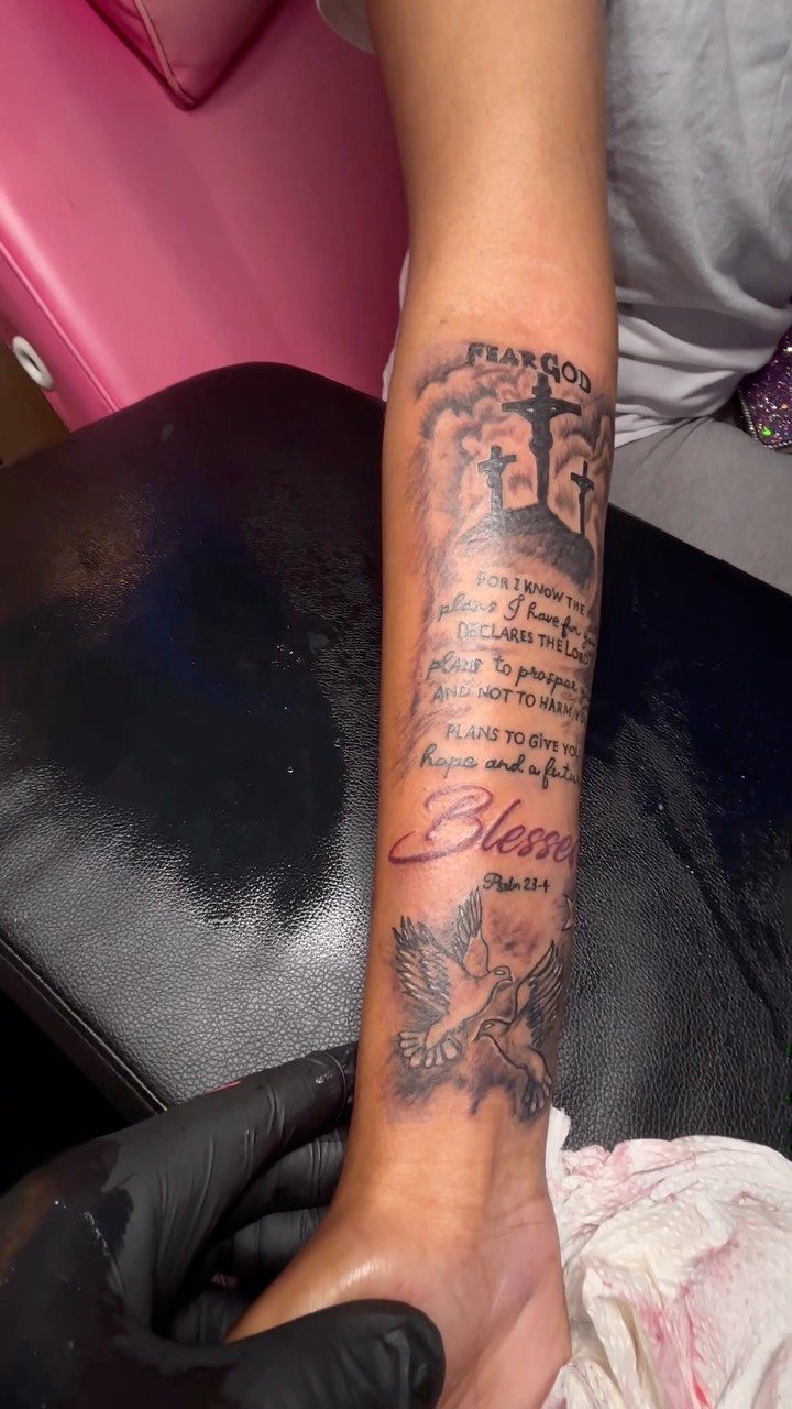 A forearm tattoo featuring religious crosses, scripture text, the word Blessed, and a dove.