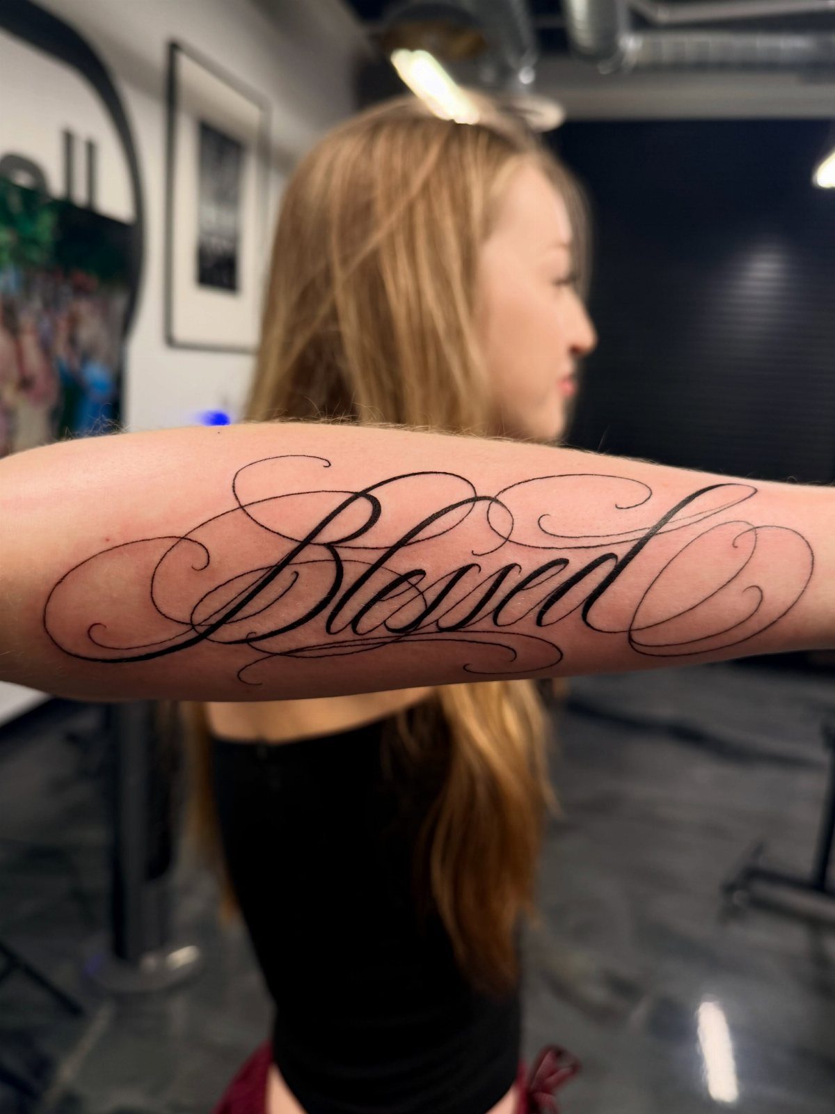 A forearm featuring a large, elegant black script tattoo that reads Blessed with decorative swirls.