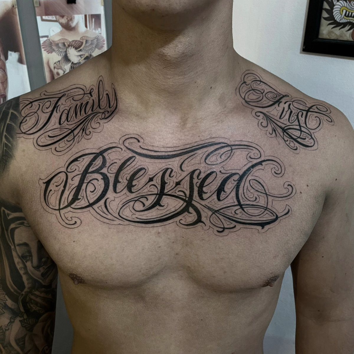 Large black script tattoos reading Family, Blessed, and First on a man's chest and shoulders.