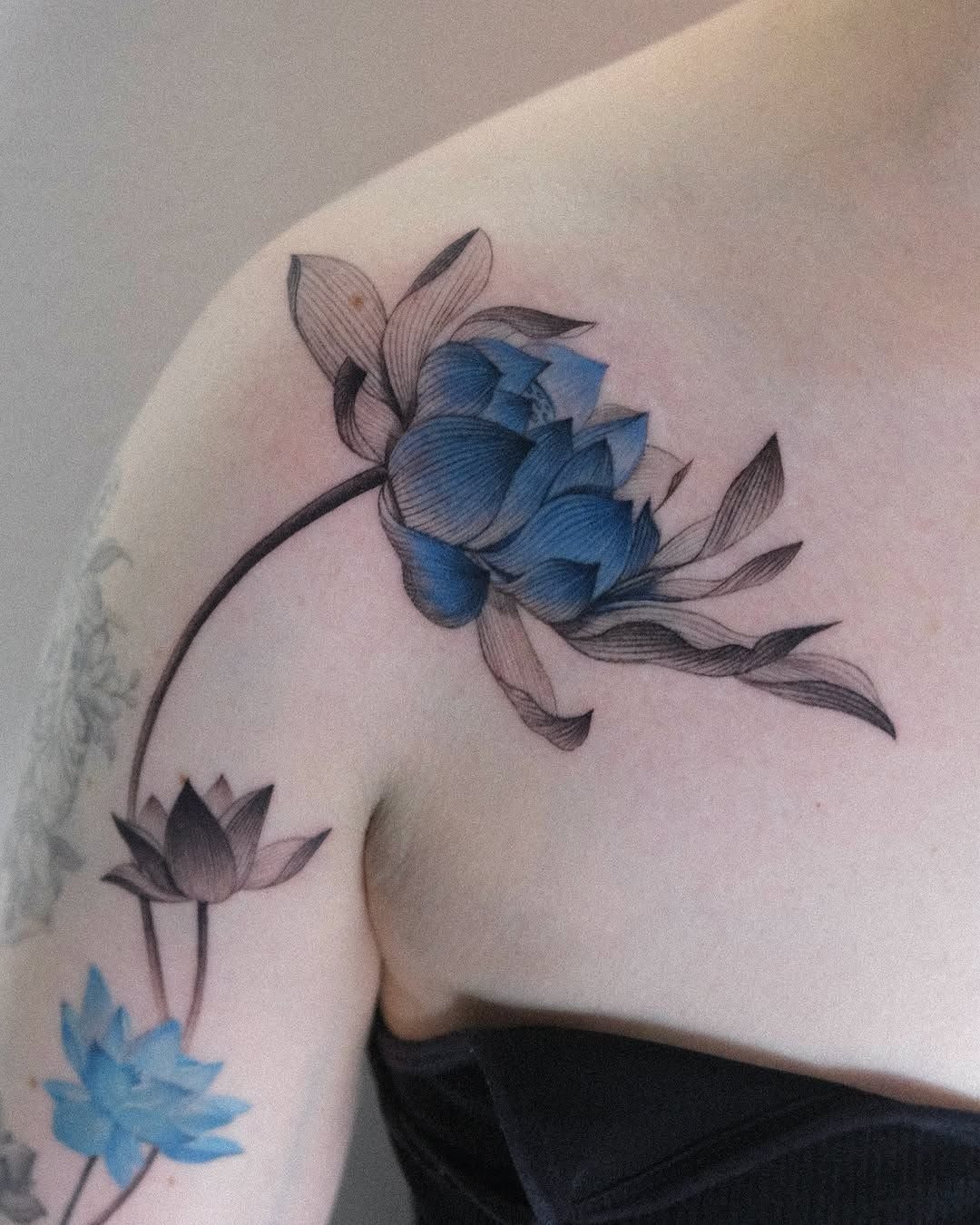 Blue lotus tattoos with black ink outlines and shading on a person's shoulder.
