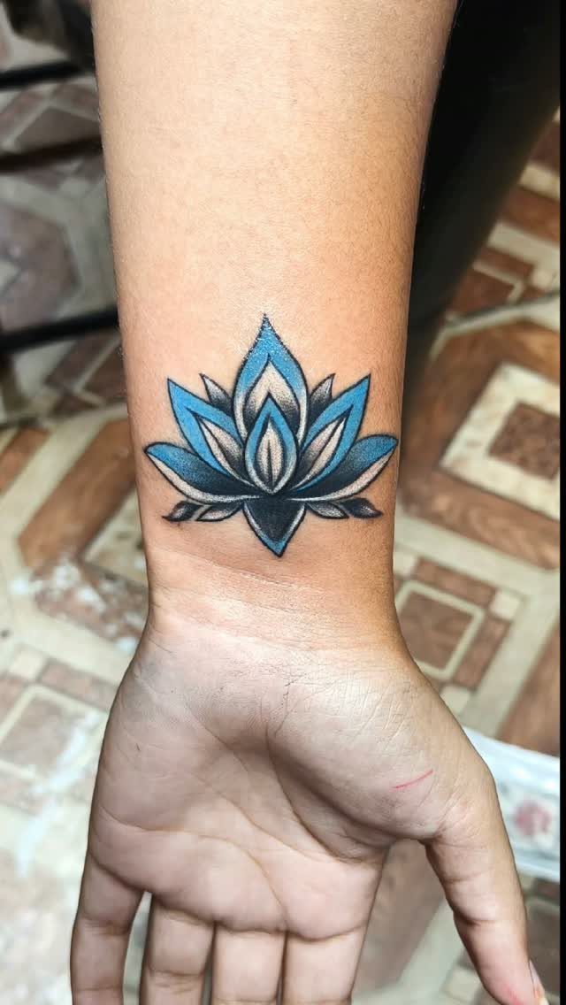 A blue and black lotus flower tattoo on a person's inner wrist.