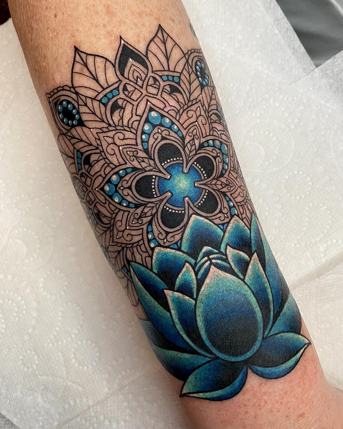 A blue lotus flower tattoo with an intricate mandala design on a person's arm.