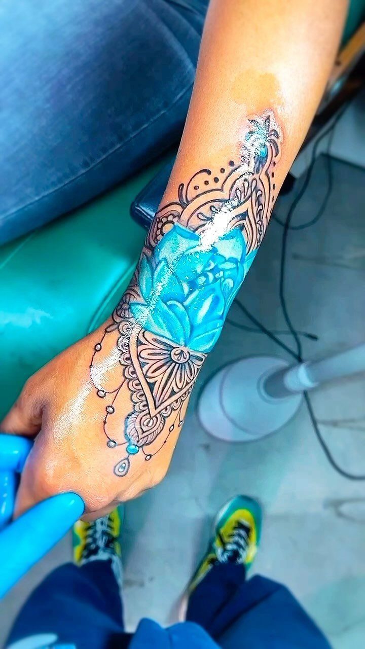 A large blue lotus tattoo with black mandala patterns on a person's forearm and hand.
