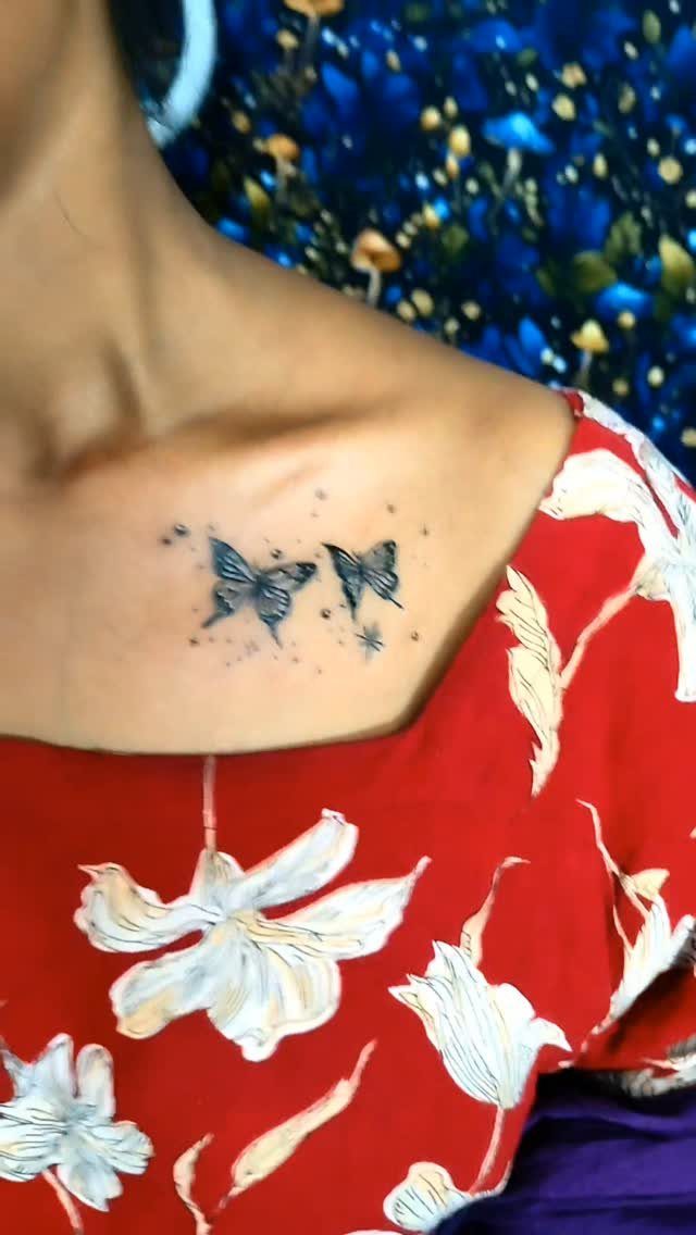 Two small black butterfly tattoos on a person's collarbone against a red floral shirt.