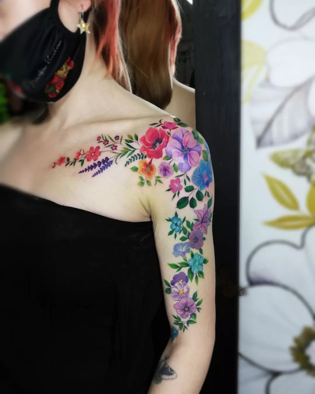 A person displaying a vibrant, colorful floral branch tattoo along their collarbone and upper arm.