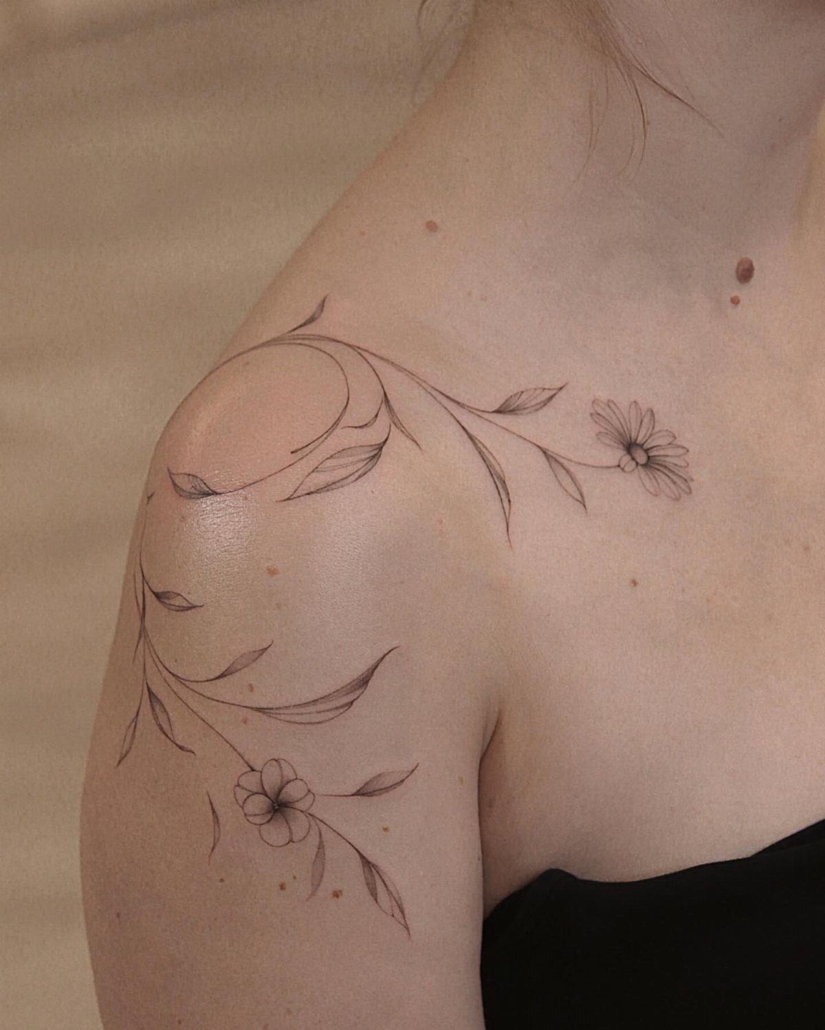 Fine line floral swirl tattoo with small flowers and leaves on a person's collarbone.