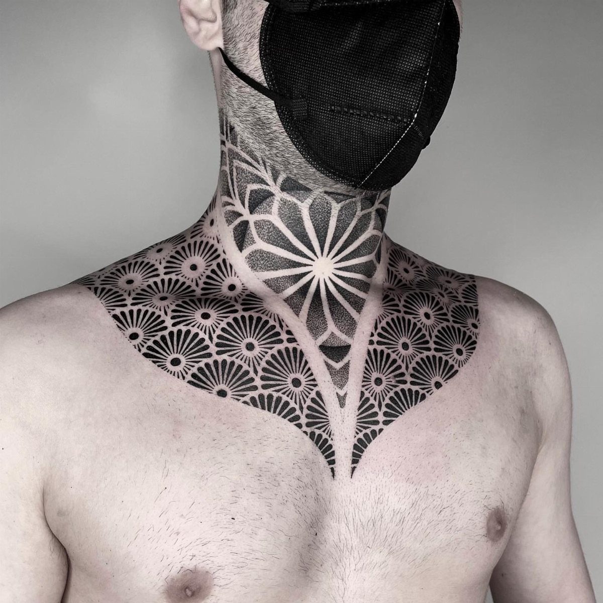 Man with a large black geometric pattern tattoo covering his neck and collarbone area.