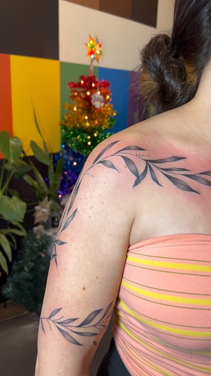 A person with black ink leaf branch tattoos on their shoulder and arm.