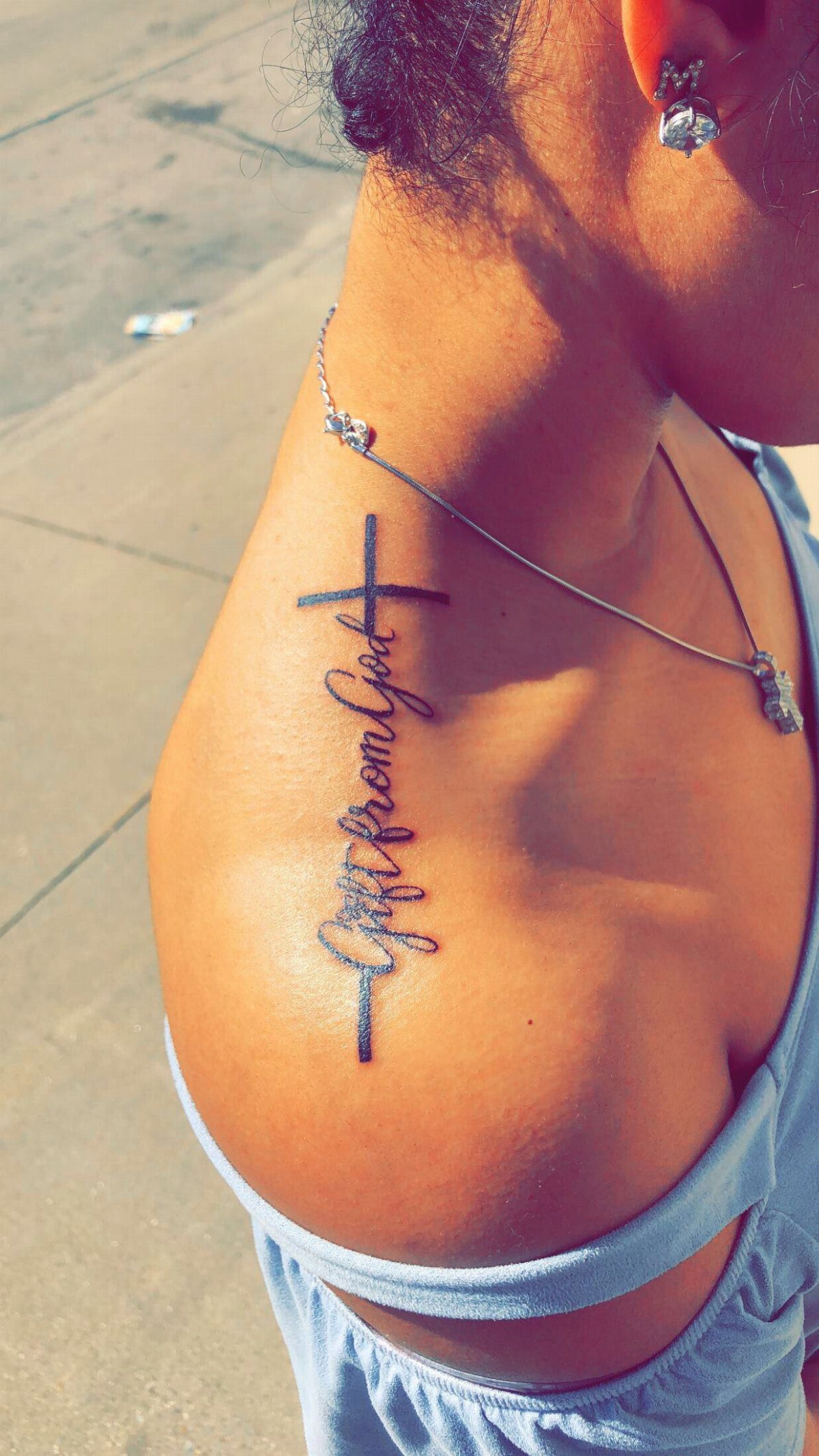 Cross tattoo with text 'gift from God' on a person's collarbone and shoulder.