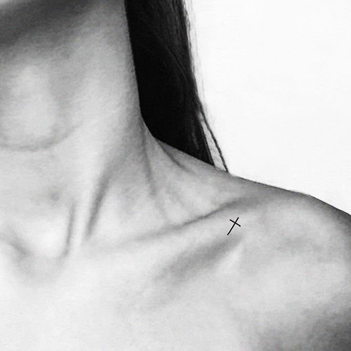 Small minimalist cross tattoo with clean lines on a person's collarbone.
