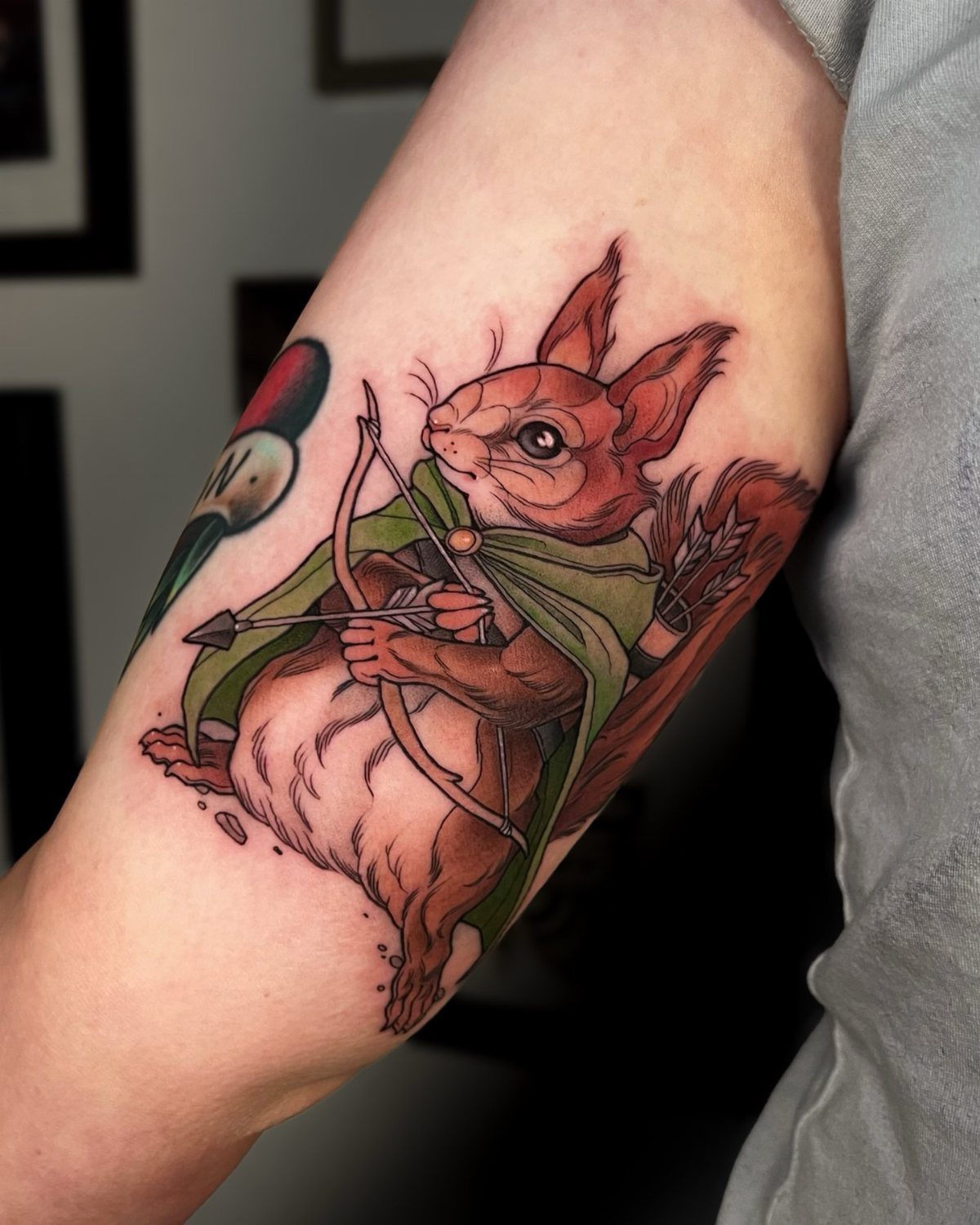 D&D Magic Tattoo Ideas: 9 Designs for Every Player 8 A detailed tattoo of a squirrel archer wearing a green cloak on a person's arm.