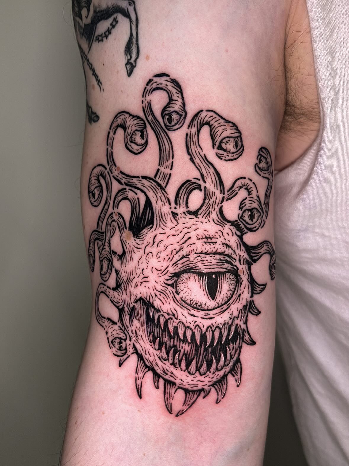 D&D Magic Tattoo Ideas: 9 Designs for Every Player 7 A detailed black ink tattoo of a many-tentacled monster with one large eye on an arm.