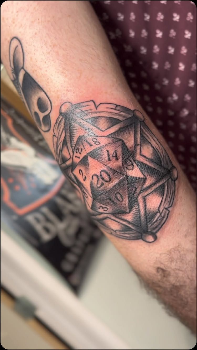 D&D Magic Tattoo Ideas: 9 Designs for Every Player 5 A black and grey tattoo of a twenty-sided die inside a geometric circular design on a forearm.