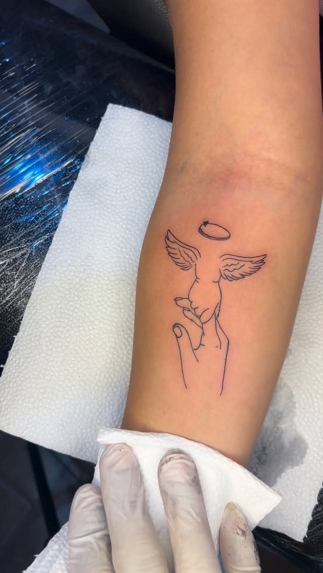 6 Evil Angel Tattoo Design Ideas and Inspiration 4 Minimalistic angel tattoo with wings and a halo being held by a hand on a forearm.