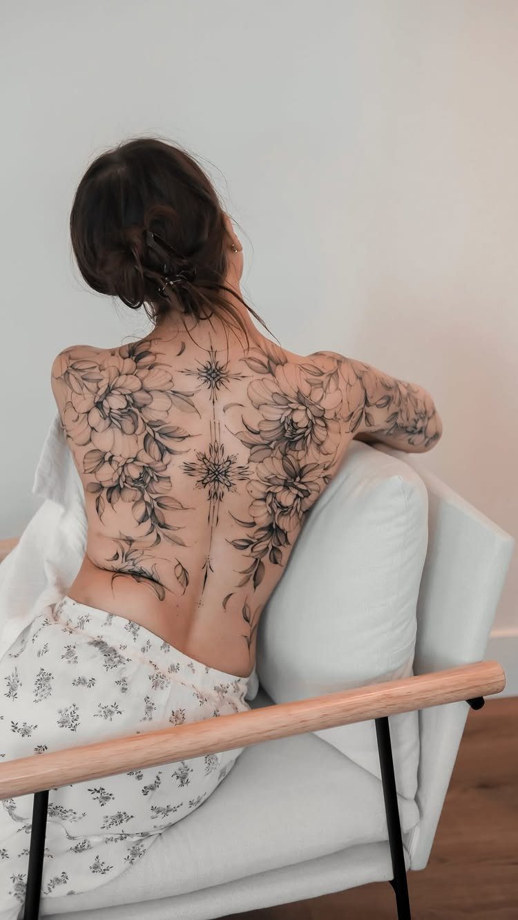 Feminine Fine Line Tattoo: 7 Ideas for Your Next Piece 2 A woman's back featuring a large, detailed fine line floral tattoo with various flowers and leaves.