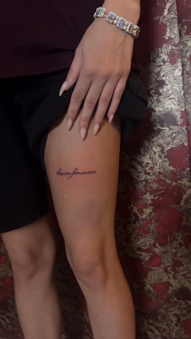 Feminine Fine Line Tattoo: 7 Ideas for Your Next Piece 7 A small cursive script tattoo on a person's upper thigh next to their hand.