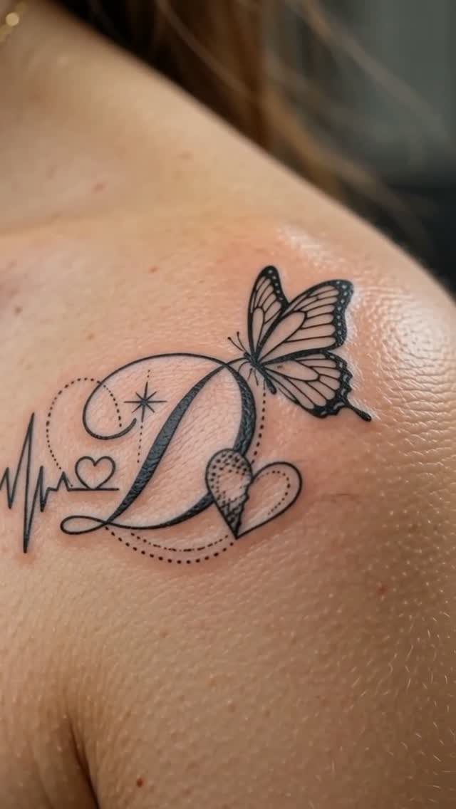 Feminine Fine Line Tattoo: 7 Ideas for Your Next Piece 4 A fine line tattoo on a shoulder featuring a butterfly, a letter D, and a heart.