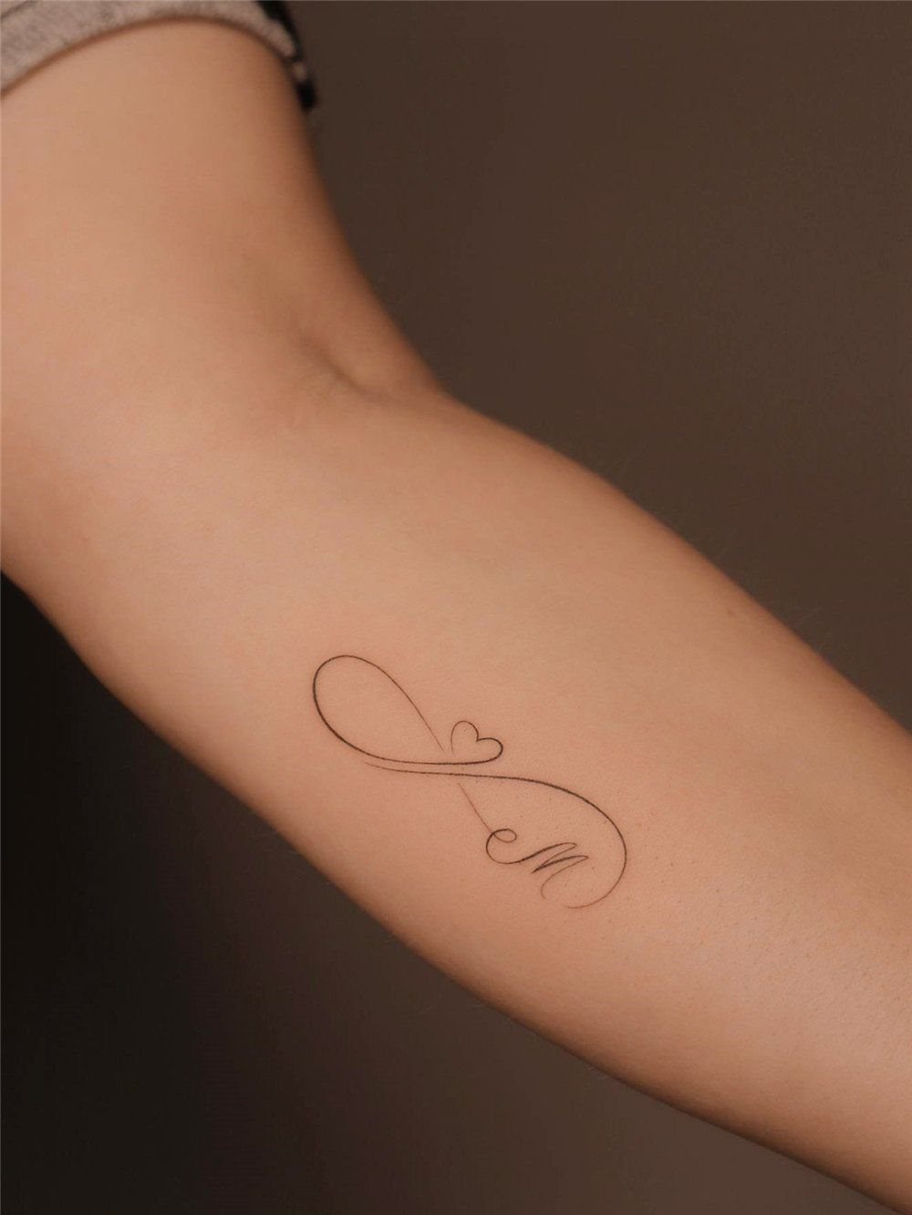Feminine Fine Line Tattoo: 7 Ideas for Your Next Piece 3 A minimalist fine line tattoo of an infinity symbol with a heart on a person's arm.