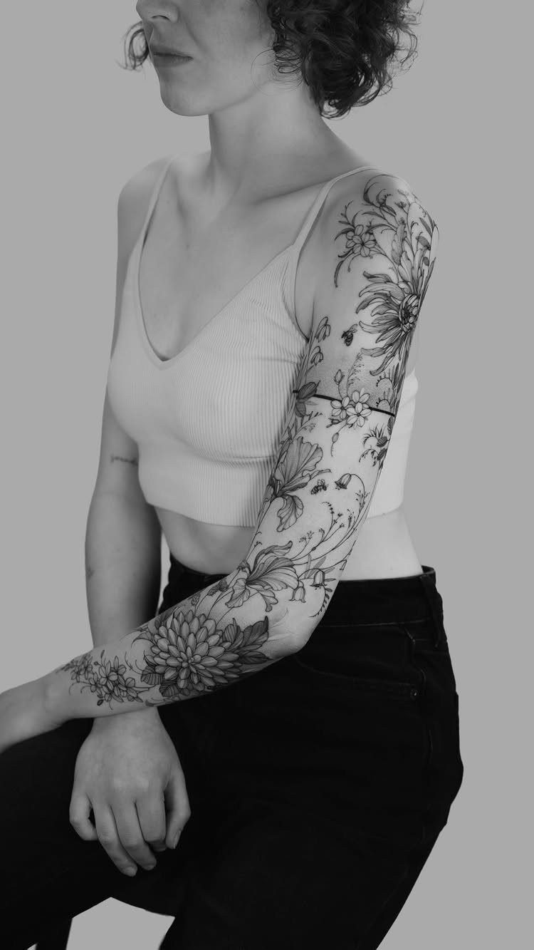 Fine Line Tattoo Sleeve: 10 Ideas With Photos 1 A woman's arm displaying a detailed black and white botanical fine line tattoo sleeve.