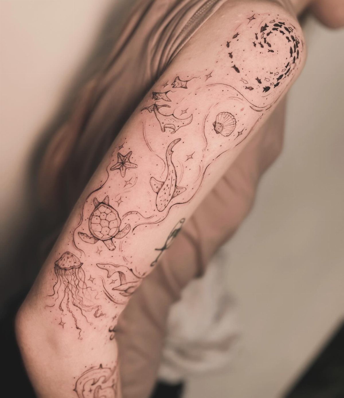 Fine Line Tattoo Sleeve: 10 Ideas With Photos 4 A person's arm displaying a fine line tattoo sleeve with jellyfish, sea turtles, and marine elements.