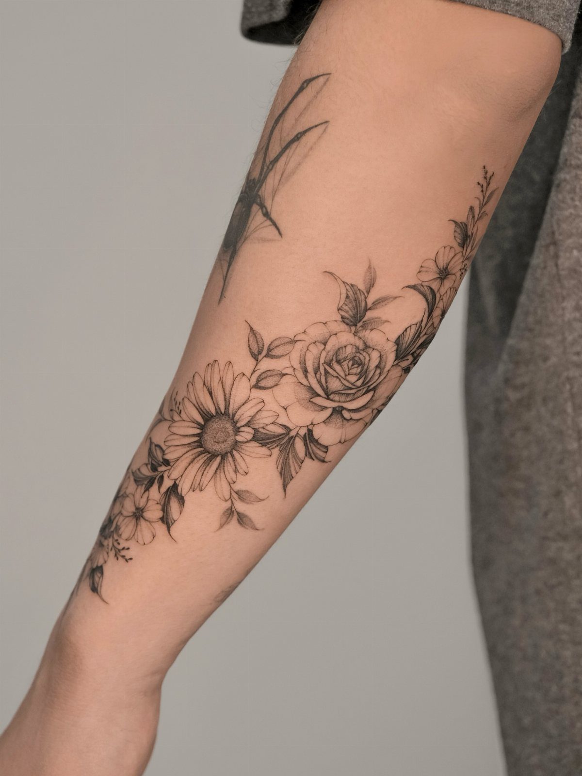 Black ink floral tattoo with a large rose and sunflower on a person's forearm.
