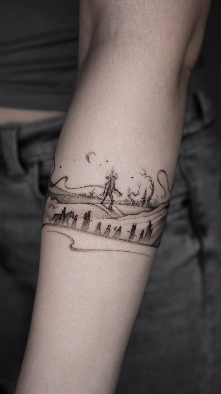 11 Forest Theme Tattoo Ideas: Wolf, Mountain, Sleeve & More 8 A black ink landscape tattoo encircling a person's forearm featuring trees and a crescent moon.