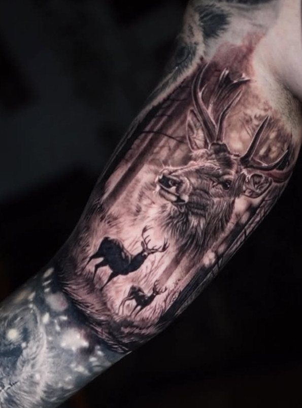 11 Forest Theme Tattoo Ideas: Wolf, Mountain, Sleeve & More 5 A detailed black and grey forest tattoo on an arm featuring deer and tall trees.