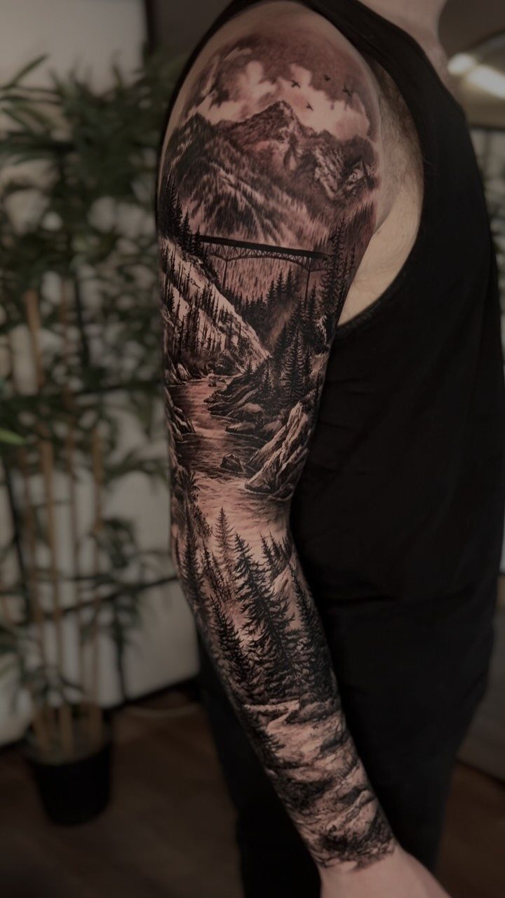 11 Forest Theme Tattoo Ideas: Wolf, Mountain, Sleeve & More 2 A detailed black and grey forest landscape sleeve tattoo covering a person's entire arm.