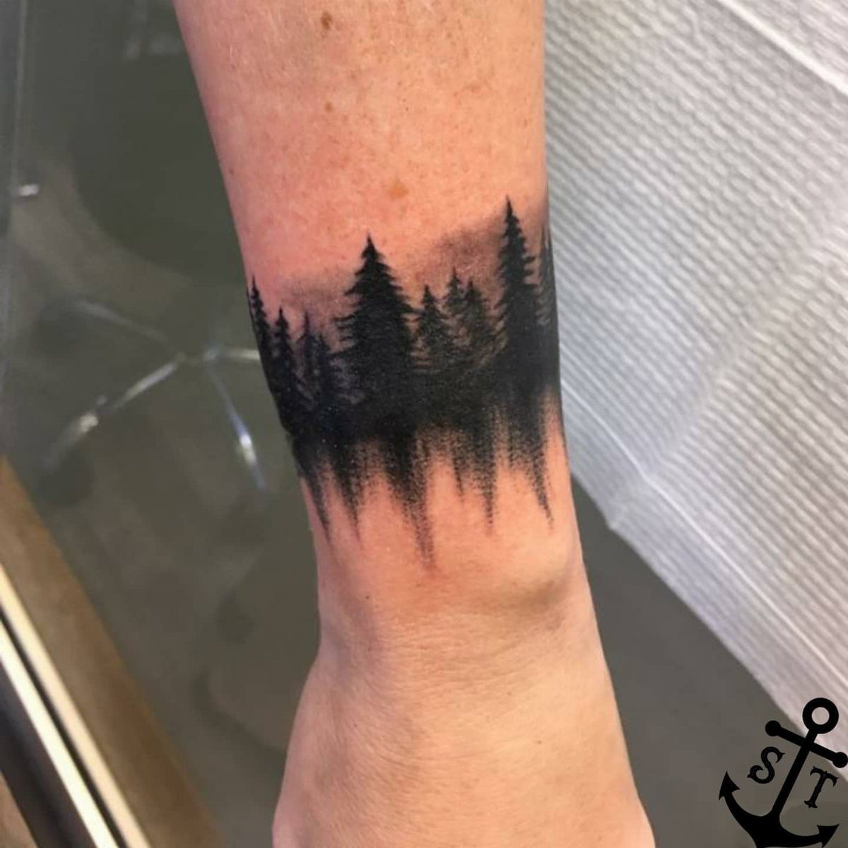 11 Forest Theme Tattoo Ideas: Wolf, Mountain, Sleeve & More 6 A black ink forest silhouette tattoo wrapping around a person's wrist.