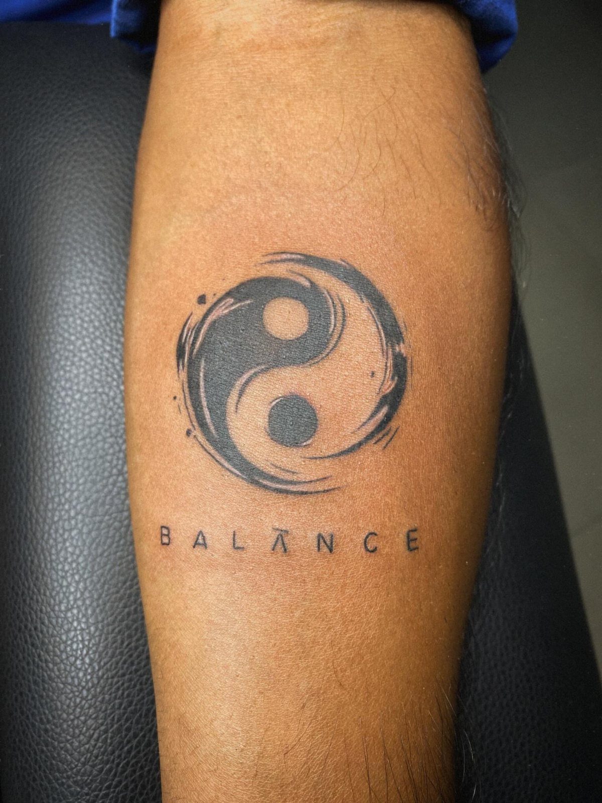 Good vs Evil Tattoo: 8 Designs That Split Skin Between Sides 5 A black ink yin-yang tattoo with the word balance printed underneath on skin.