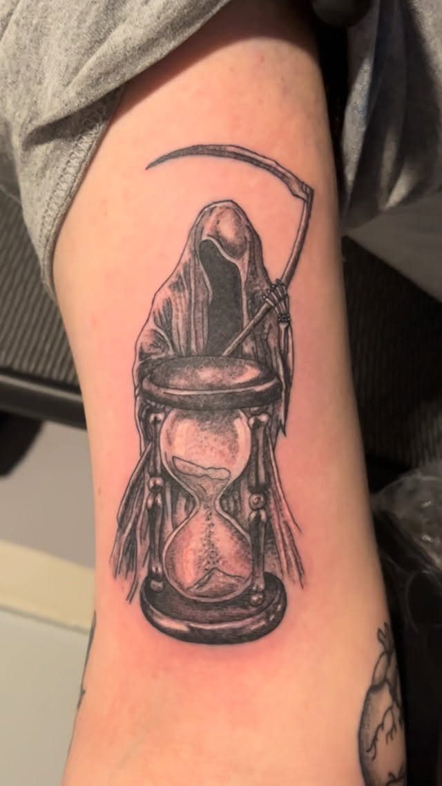 Hour Glass Tattoo Ideas: 12 Designs for Every Style 4 A black and grey tattoo of the Grim Reaper standing behind a detailed hourglass on skin.