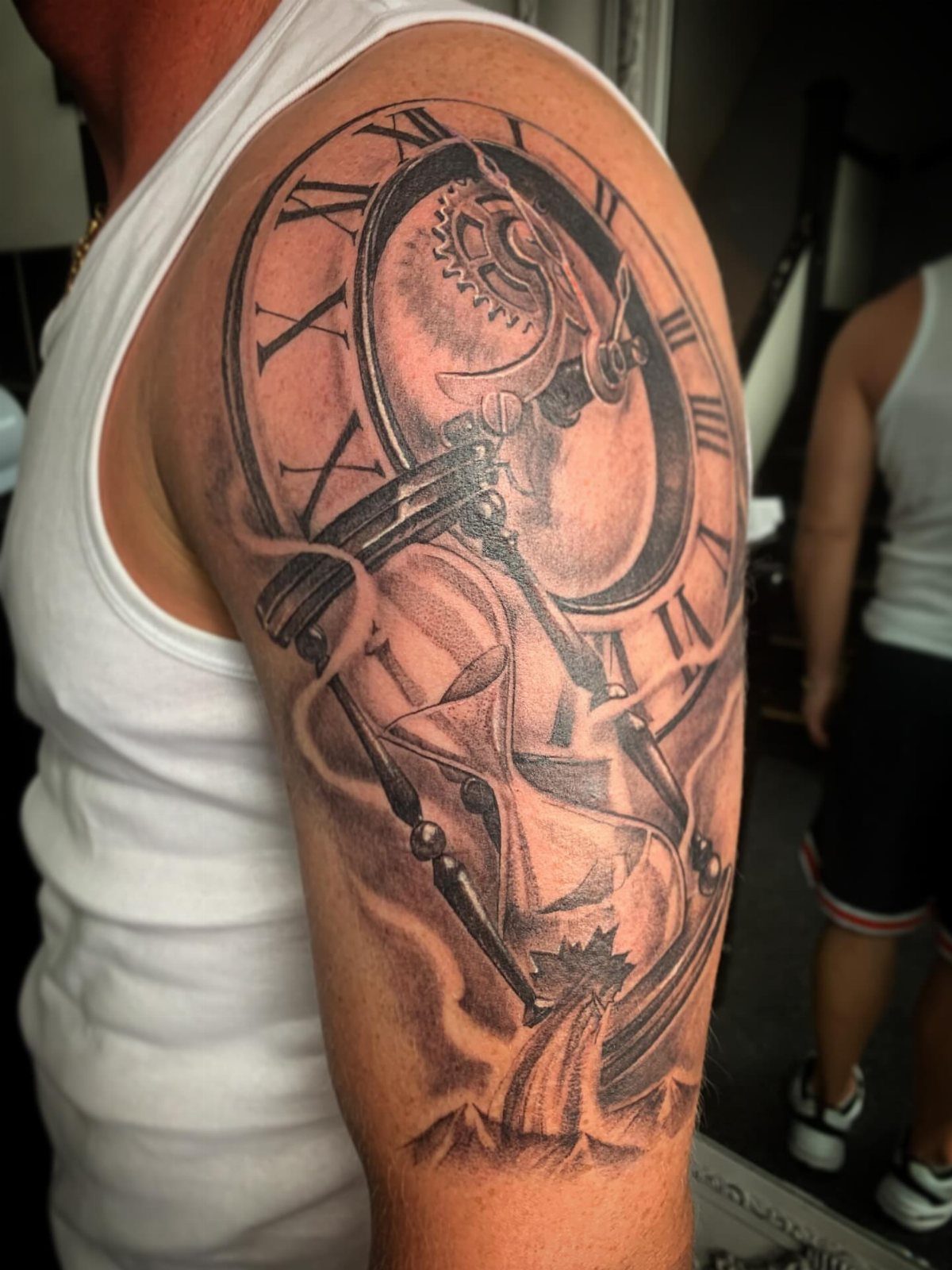Hour Glass Tattoo Ideas: 12 Designs for Every Style 6 A large black and grey realism tattoo of a broken hourglass and clock face on a person's arm.