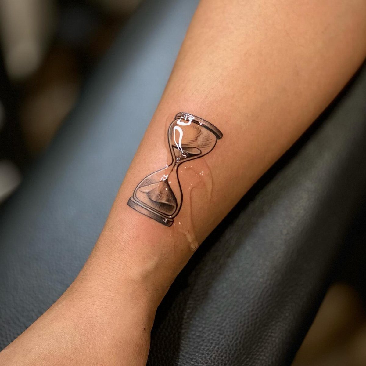 Hour Glass Tattoo Ideas: 12 Designs for Every Style 2 A realistic black and grey hourglass tattoo on a person's forearm skin.