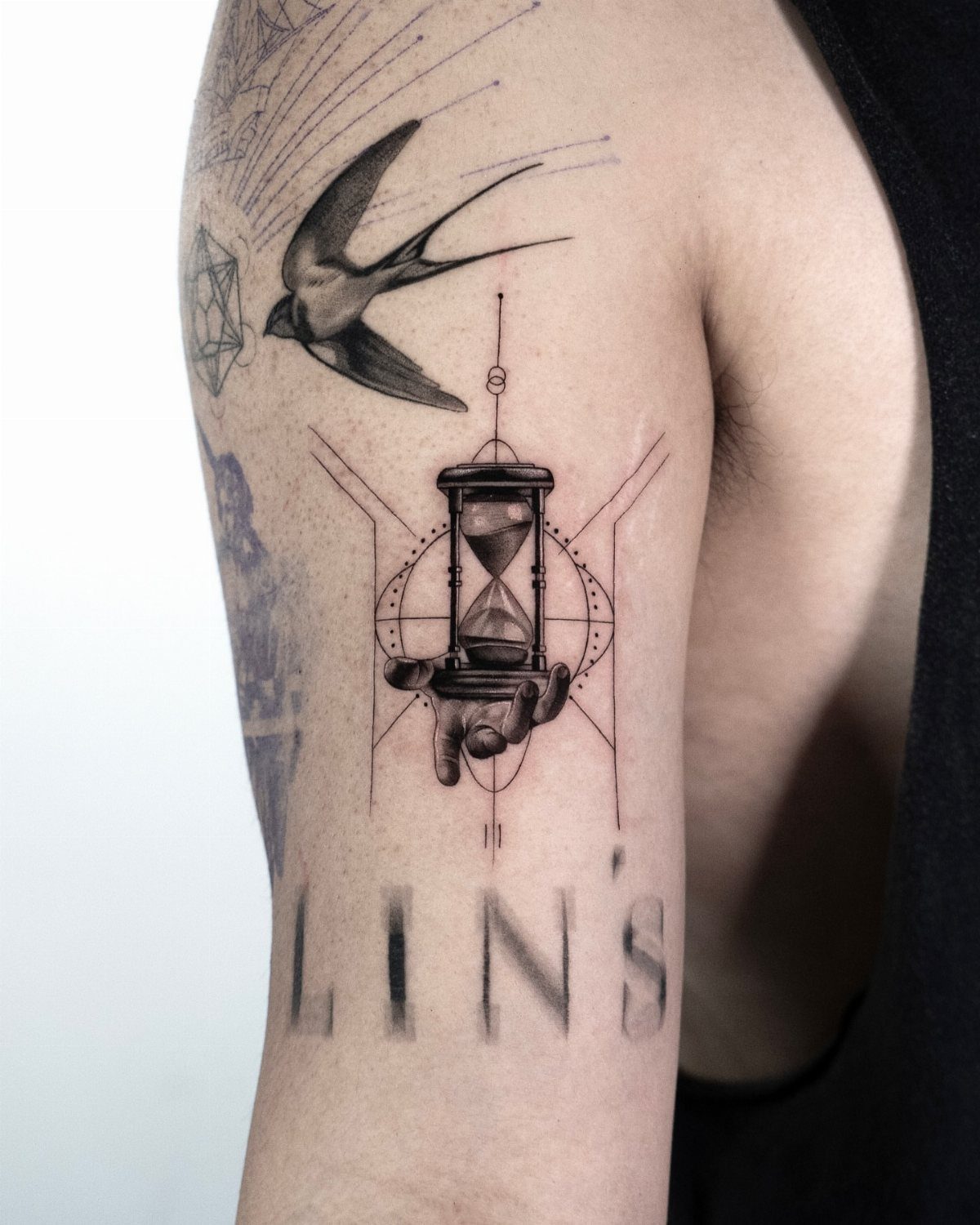 Hour Glass Tattoo Ideas: 12 Designs for Every Style 11 A black and grey tattoo on an arm featuring an hourglass, a hand, and a swallow bird.