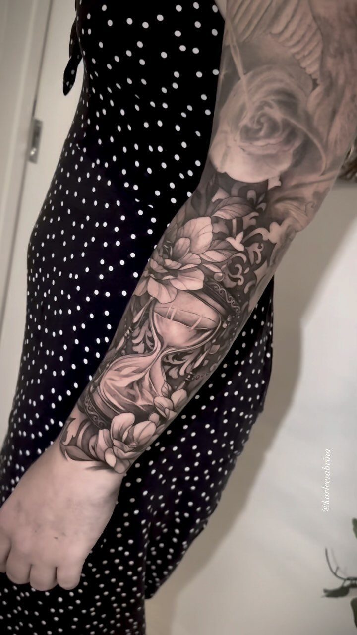Hour Glass Tattoo Ideas: 12 Designs for Every Style 7 A detailed black and grey realism tattoo of an hourglass and roses on a person's forearm.
